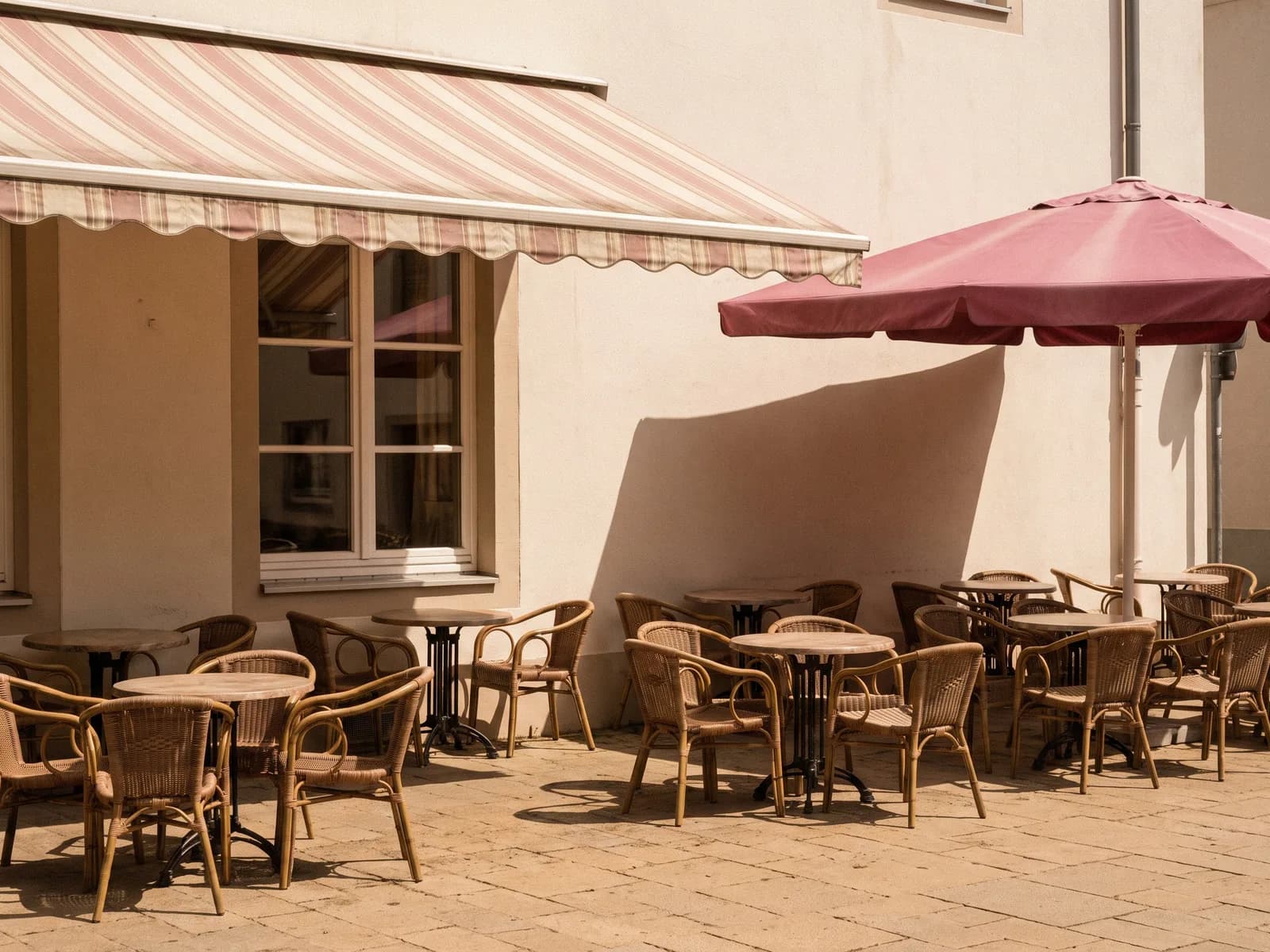 Terrasse eines Eiscafés im Sommer: Korbstühle, gestreifte Markise, ein Sonnenschirm